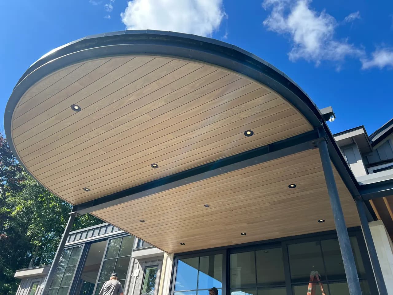Curved wood-slat soffit ceiling with recessed lighting over a covered modern patio by JTL Projects