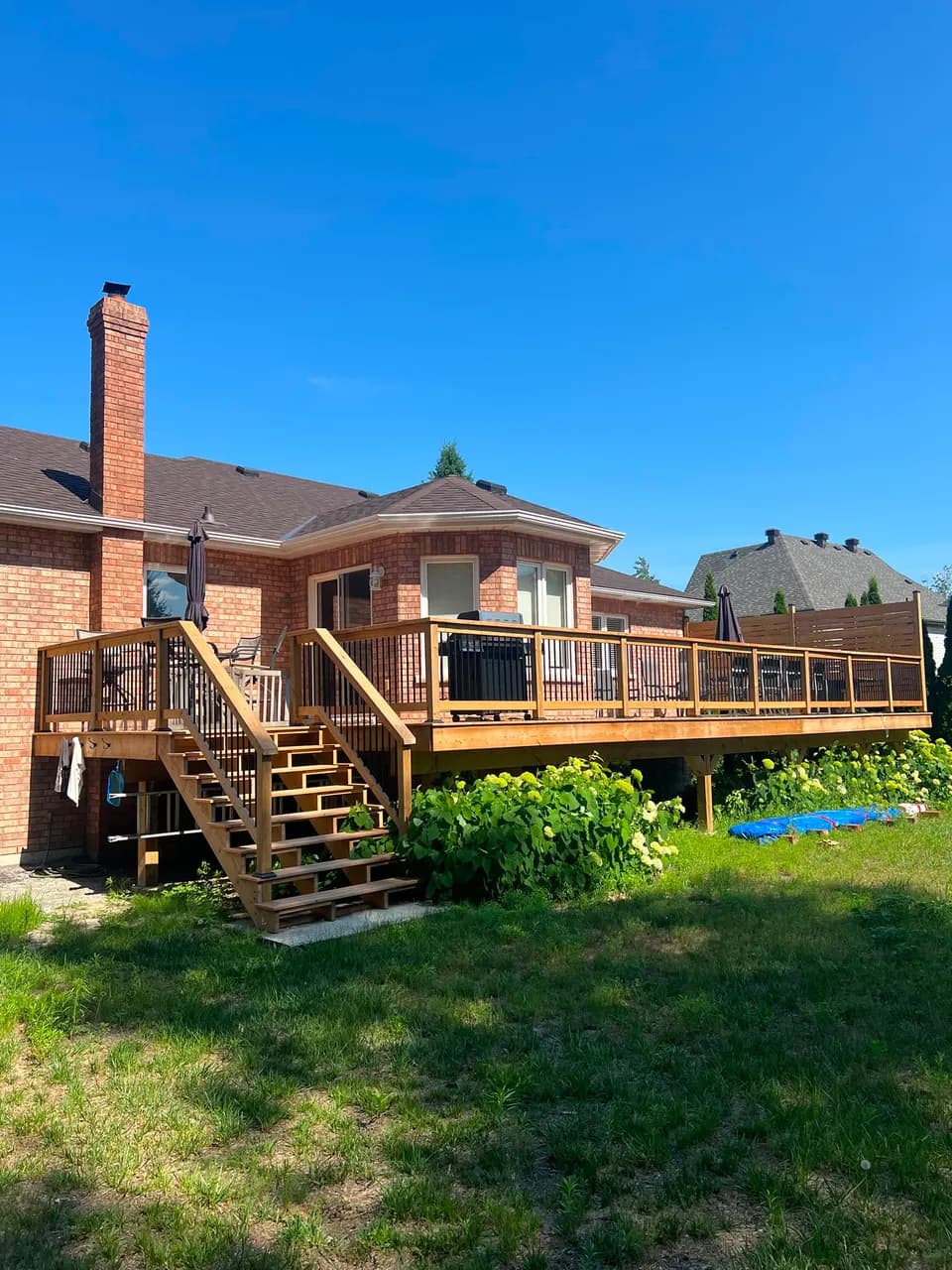 Raised backyard deck with staircase, black-baluster railings, and privacy screen on a brick home by JTL Projects